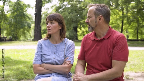 A middle-aged man tries to talk to an angry middle-aged woman in a park on a sunny day