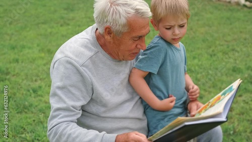 Happy grandfather reading book to curious grandson outdoors. Close up. Grandpa with grandchild spending time together. Family time comes in various forms. 4s year boy and senior man read story in park photo