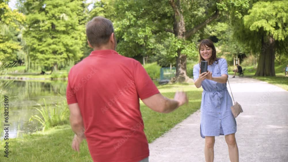 A middle-aged Caucasian couple has fun taking videos with a smartphone as the man does a goofy dance in a park on a sunny day A middle-aged Caucasian couple has fun taking videos with a smartphone as the man does a goofy dance in a park on a sunny day
