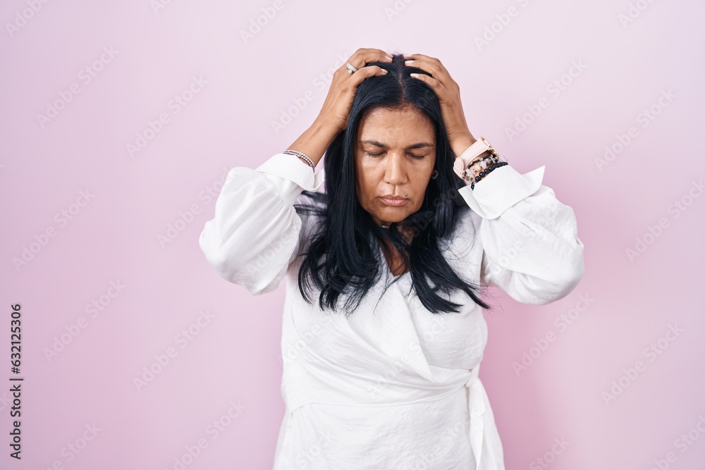 Mature hispanic woman standing over pink background suffering from headache desperate and stressed because pain and migraine. hands on head. Mature hispanic woman standing over pink background suffering from headache desperate and stressed because pain and migraine. hands on head.