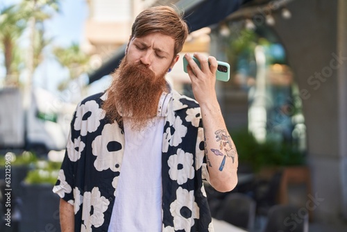 Young redhead man listening audio message by sthe smartphone at street photo