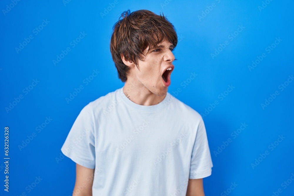 Obraz premium Hispanic young man standing over blue background angry and mad screaming frustrated and furious, shouting with anger. rage and aggressive concept.