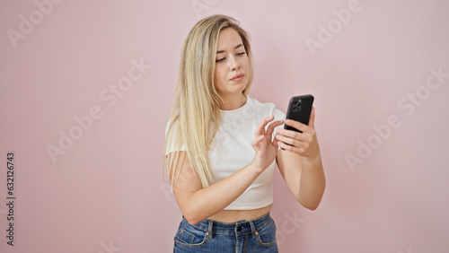 Young blonde woman using smartphone with serious expression over isolated pink background