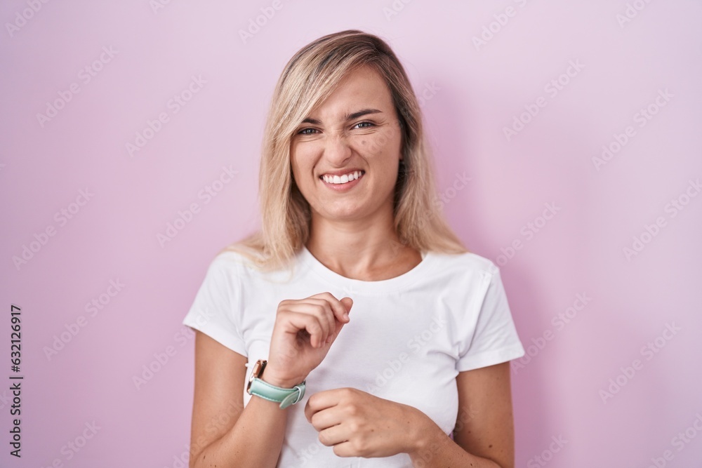 Young blonde woman standing over pink background disgusted expression, displeased and fearful doing disgust face because aversion reaction. Young blonde woman standing over pink background disgusted expression, displeased and fearful doing disgust face because aversion reaction.