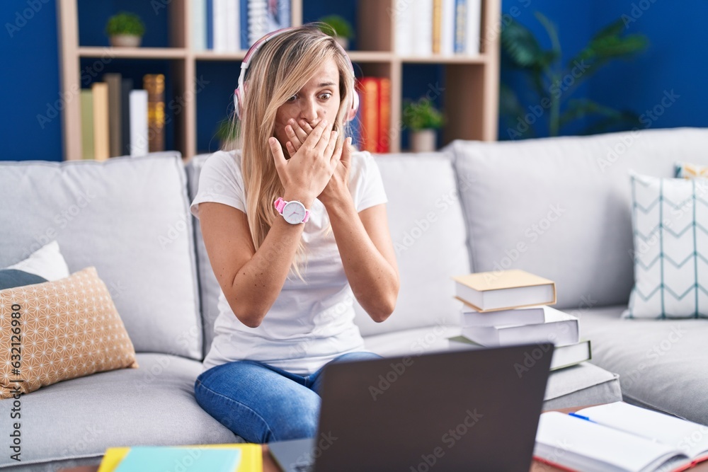 Young blonde woman studying using computer laptop at home shocked covering mouth with hands for mistake. secret concept. Young blonde woman studying using computer laptop at home shocked covering mouth with hands for mistake. secret concept.