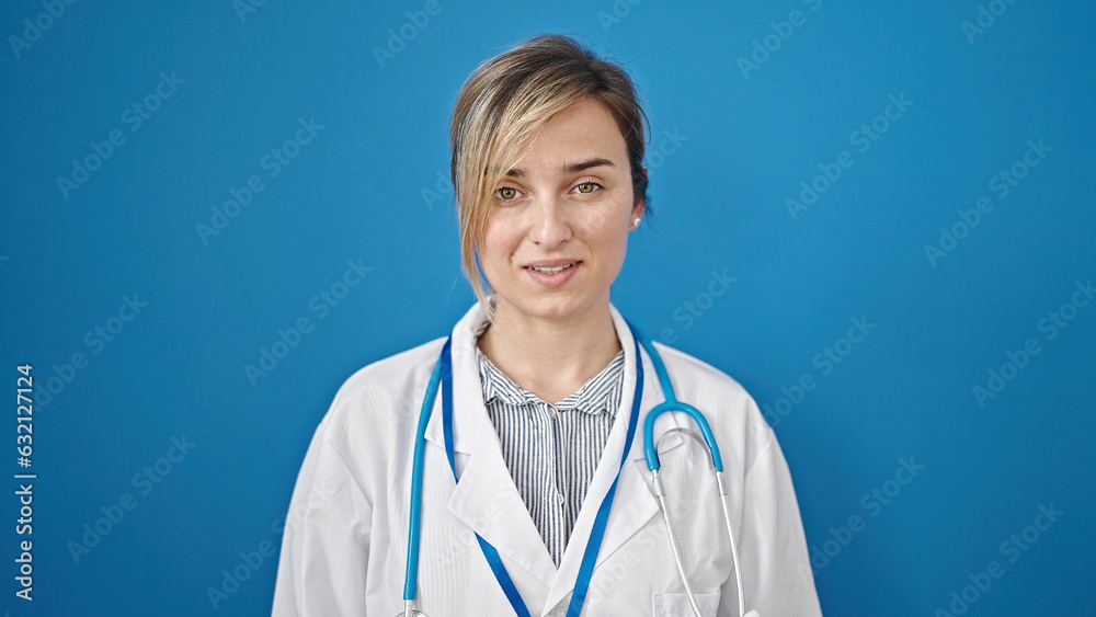 Young blonde woman doctor smiling confident standing over isolated blue background Young blonde woman doctor smiling confident standing over isolated blue background