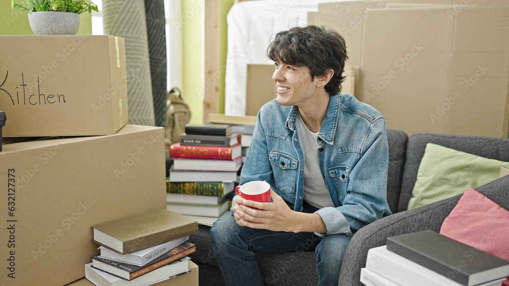 Young hispanic man drinking coffee sitting on sofa at new home Young hispanic man drinking coffee sitting on sofa at new home