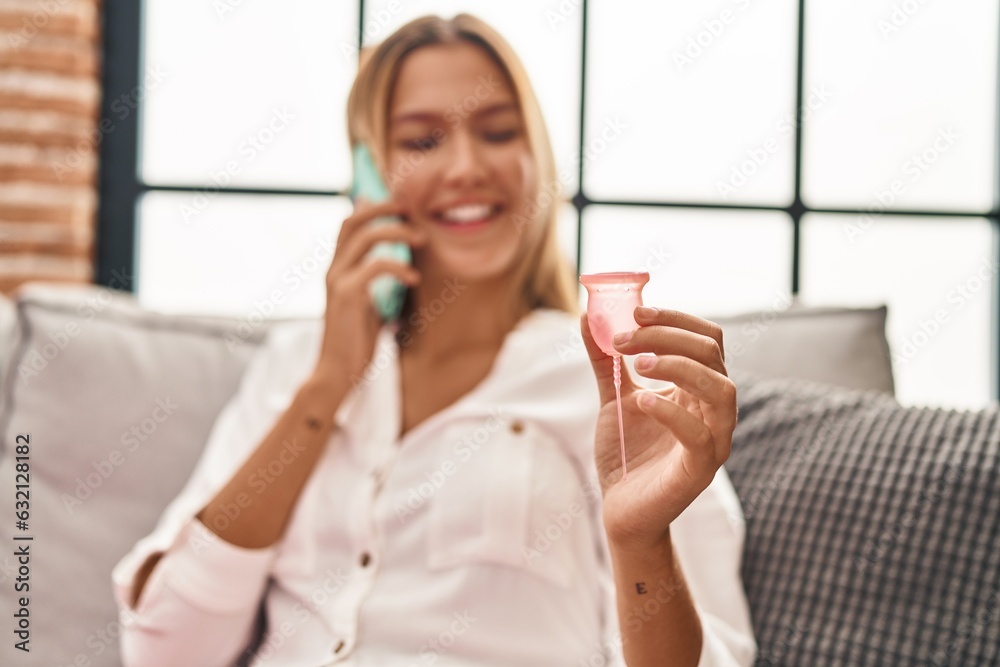 Young hispanic woman talking on smartphone holding menstrual cup at home Young hispanic woman talking on smartphone holding menstrual cup at home