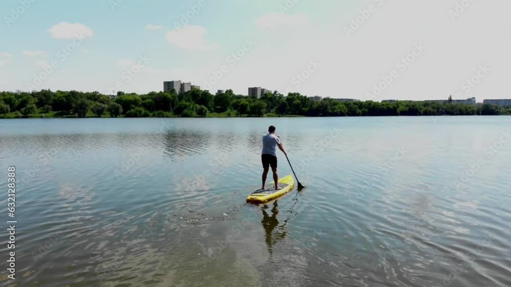 Drone view of a young guy paddling a SUP board on a beautiful lake in northern Europe. A guy with a paddle on a SUP board floats on a lake in Ukraine in the city of Sumy Drone view of a young guy paddling a SUP board on a beautiful lake in northern Europe. A guy with a paddle on a SUP board floats on a lake in Ukraine in the city of Sumy