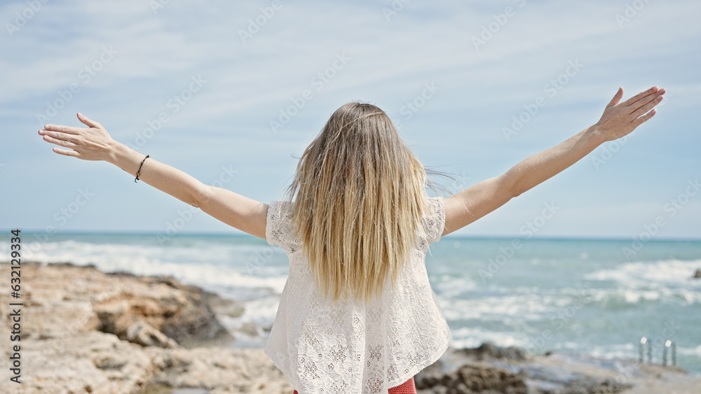 Young blonde woman tourist standing with arms open backwards at beach Young blonde woman tourist standing with arms open backwards at beach