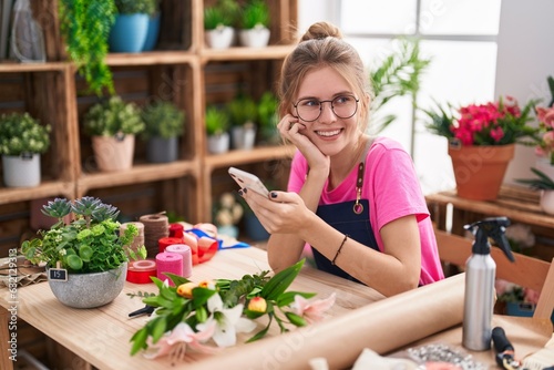 Young blonde woman florist smiling confident using smartphone at flower shop