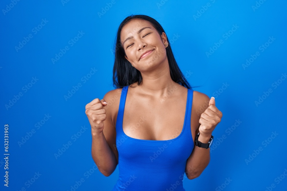 Hispanic woman standing over blue background excited for success with arms raised and eyes closed celebrating victory smiling. winner concept. Hispanic woman standing over blue background excited for success with arms raised and eyes closed celebrating victory smiling. winner concept.