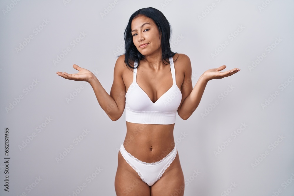 Hispanic woman wearing lingerie clueless and confused expression with arms and hands raised. doubt concept. Hispanic woman wearing lingerie clueless and confused expression with arms and hands raised. doubt concept.