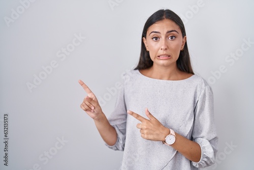 Young hispanic woman standing over white background pointing aside worried and nervous with both hands, concerned and surprised expression photo