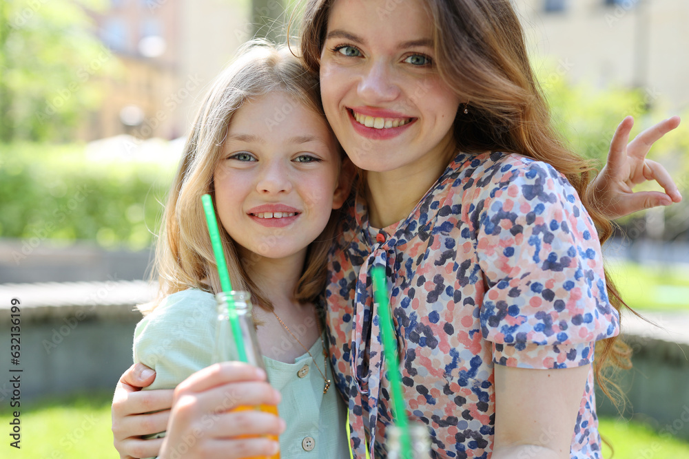 A happy mother and daughter hugging and smiling in a park. They wear green and patterned shirts and have fun with a straw and a peace sign. A happy mother and daughter hugging and smiling in a park. They wear green and patterned shirts and have fun with a straw and a peace sign.