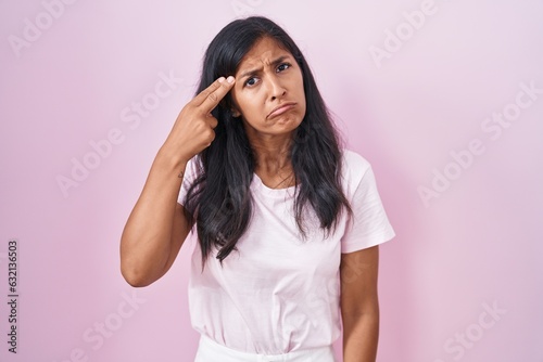 Young hispanic woman standing over pink background shooting and killing oneself pointing hand and fingers to head like gun  suicide gesture.