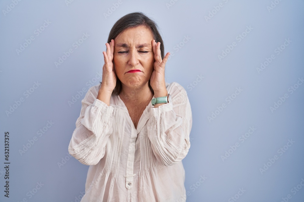Middle age hispanic woman standing over blue background with hand on head, headache because stress. suffering migraine. Middle age hispanic woman standing over blue background with hand on head, headache because stress. suffering migraine.