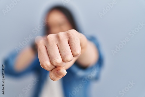 Hispanic woman standing over blue background punching fist to fight, aggressive and angry attack, threat and violence