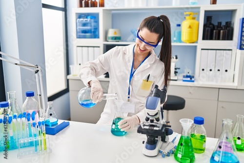 Young beautiful hispanic woman scientist pouring liquid on test tube at laboratory