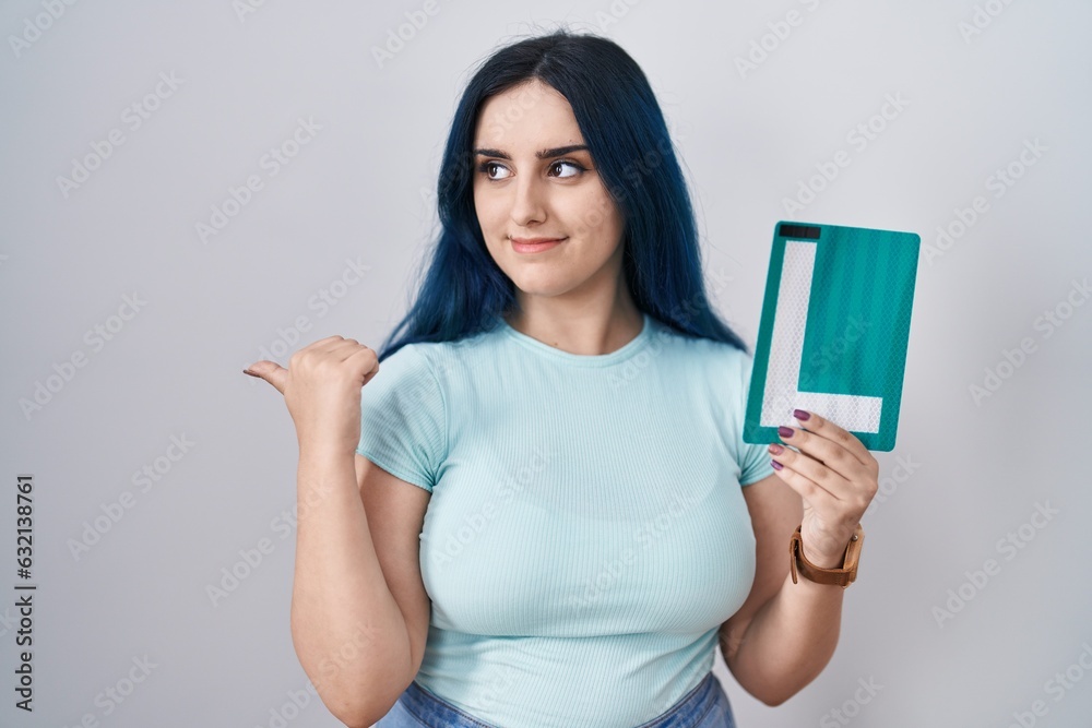 Young modern girl with blue hair holding l sign for new driver pointing thumb up to the side smiling happy with open mouth Young modern girl with blue hair holding l sign for new driver pointing thumb up to the side smiling happy with open mouth