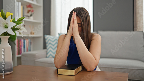 Young beautiful hispanic woman praying sitting on floor at home