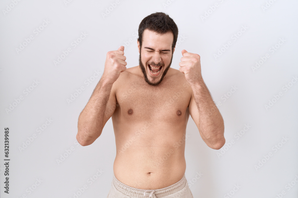 Young hispanic man standing shirtless over white background excited for success with arms raised and eyes closed celebrating victory smiling. winner concept.