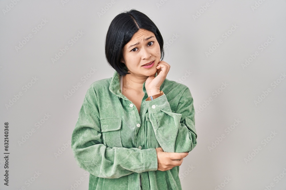 Young asian woman standing over white background thinking worried about a question, concerned and nervous with hand on chin Young asian woman standing over white background thinking worried about a question, concerned and nervous with hand on chin