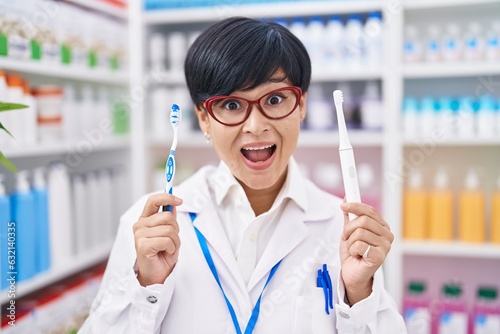 Young asian woman with short hair doing toothbrush comparative at pharmacy celebrating crazy and amazed for success with open eyes screaming excited.
