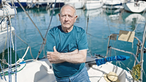 Senior grey-haired man standing with relaxed expression and arms crossed gesture at boat