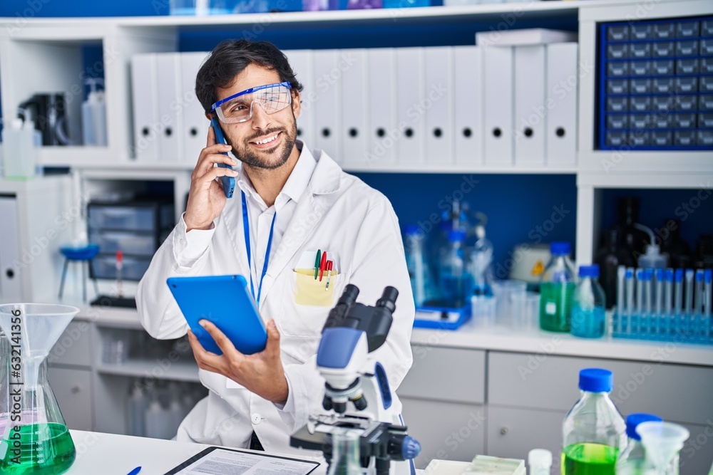 Young hispanic man scientist talking on the smartphone using touchpad at laboratory Young hispanic man scientist talking on the smartphone using touchpad at laboratory