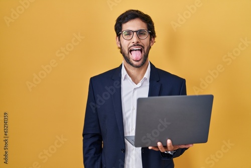 Handsome latin man working using computer laptop sticking tongue out happy with funny expression. emotion concept.