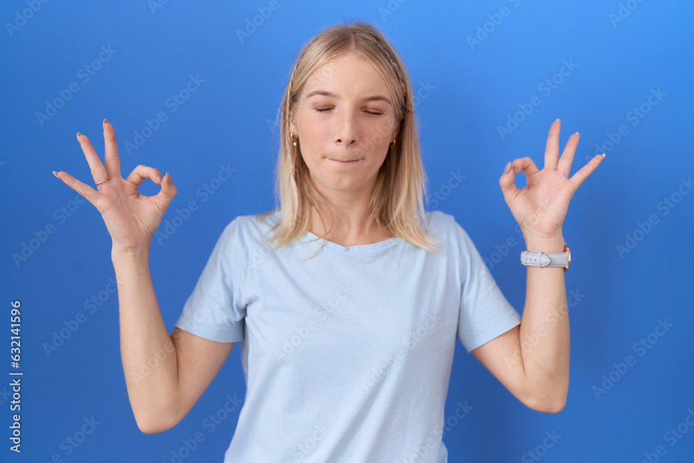 Young caucasian woman wearing casual blue t shirt relaxed and smiling with eyes closed doing meditation gesture with fingers. yoga concept. Young caucasian woman wearing casual blue t shirt relaxed and smiling with eyes closed doing meditation gesture with fingers. yoga concept.