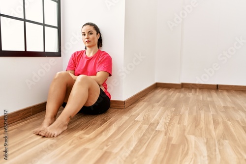 Young beautiful hispanic woman sitting on floor with serious expression at empty room