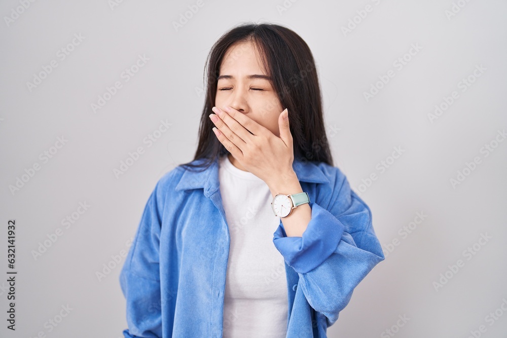 Young chinese woman standing over white background bored yawning tired covering mouth with hand. restless and sleepiness. Young chinese woman standing over white background bored yawning tired covering mouth with hand. restless and sleepiness.