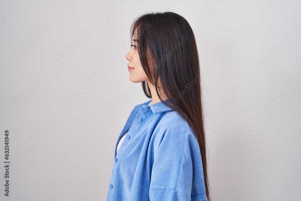 Young chinese woman standing over white background looking to side, relax profile pose with natural face and confident smile.