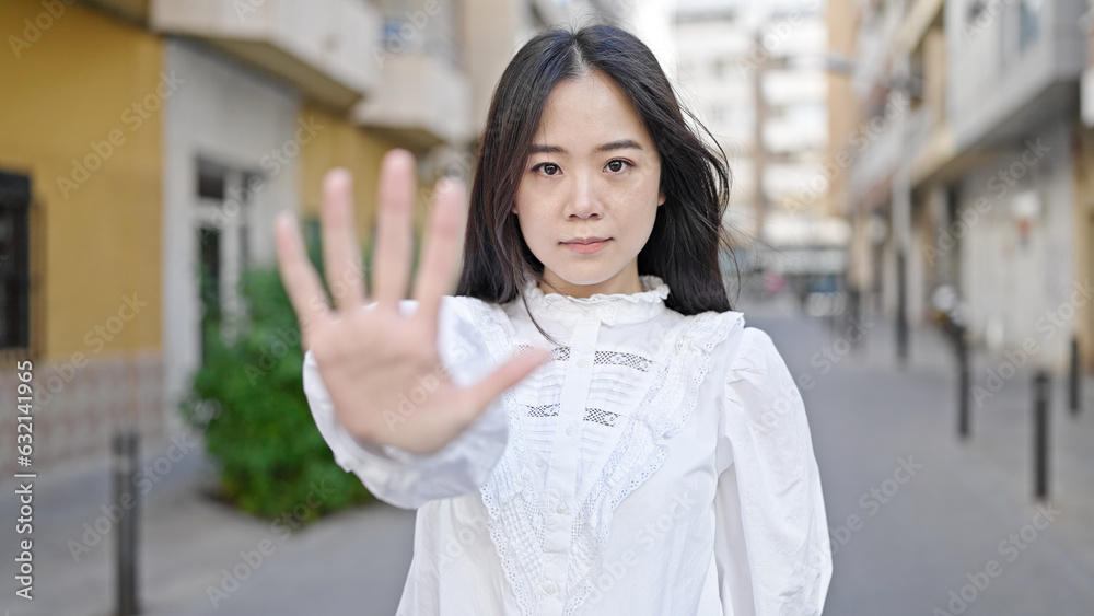 Young chinese woman doing stop gesture with hand at street
