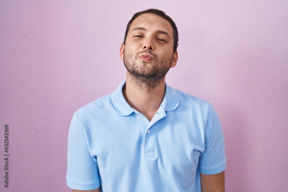Hispanic man standing over pink background looking at the camera blowing a kiss on air being lovely and sexy. love expression. Hispanic man standing over pink background looking at the camera blowing a kiss on air being lovely and sexy. love expression.