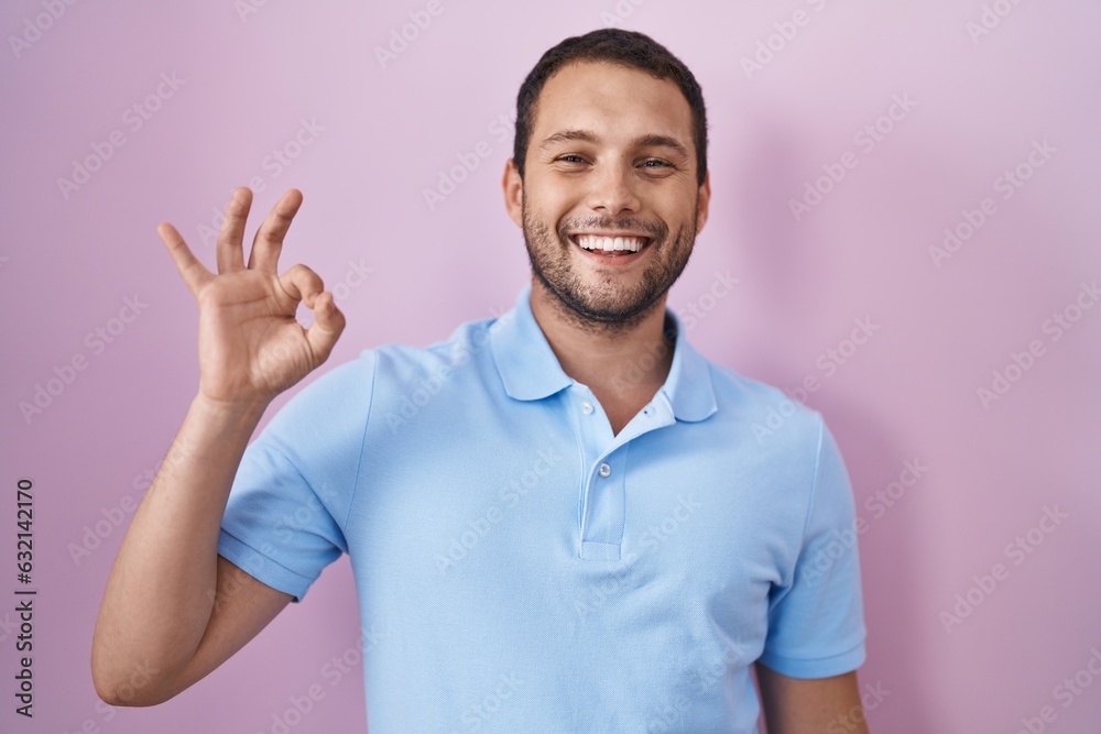 Hispanic man standing over pink background smiling positive doing ok sign with hand and fingers. successful expression. Hispanic man standing over pink background smiling positive doing ok sign with hand and fingers. successful expression.