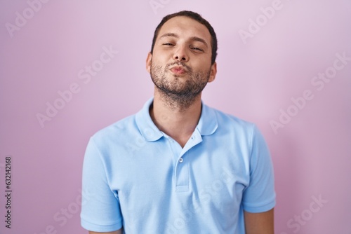 Hispanic man standing over pink background looking at the camera blowing a kiss on air being lovely and sexy. love expression.