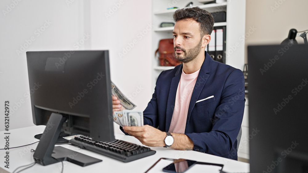 Young hispanic man business worker using computer counting dollars at office