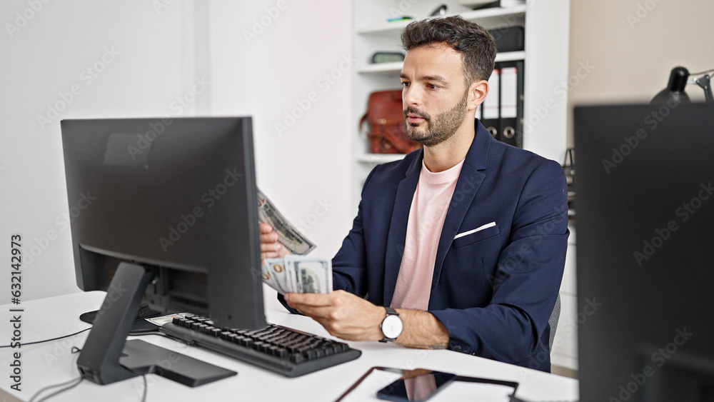 Young hispanic man business worker using computer counting dollars at office Young hispanic man business worker using computer counting dollars at office