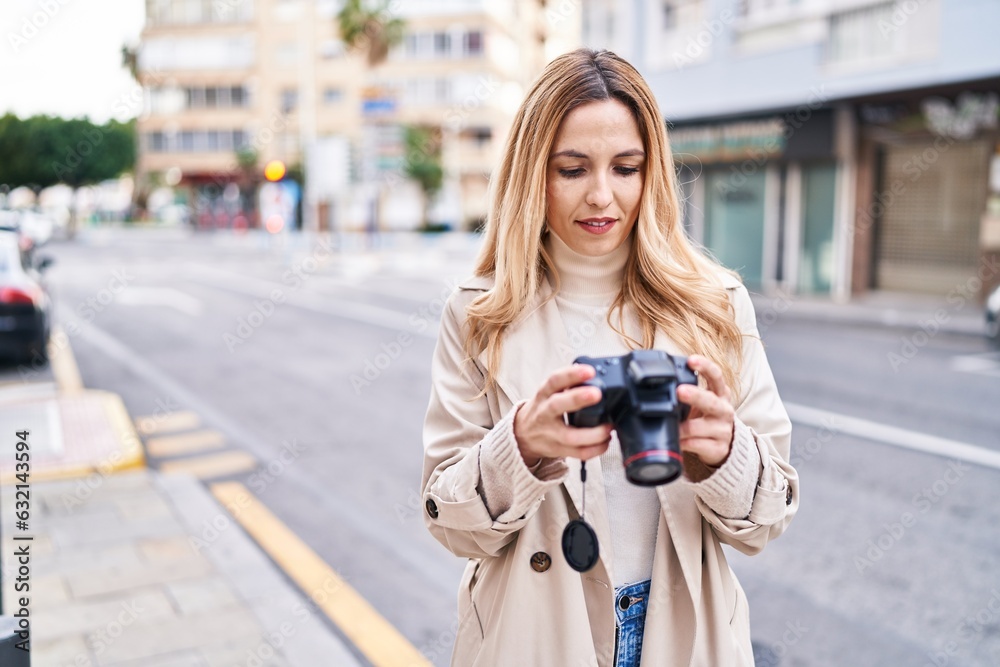 Young blonde woman smiling confident using professional camera at street
