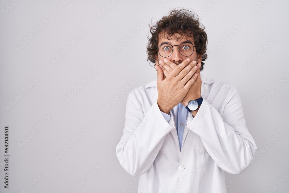 Hispanic young man wearing doctor uniform shocked covering mouth with hands for mistake. secret concept.