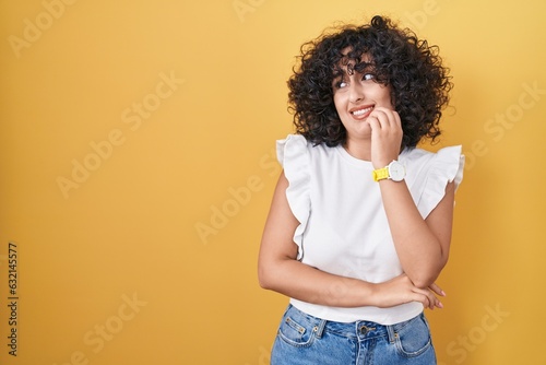 Young middle east woman standing over yellow background looking stressed and nervous with hands on mouth biting nails. anxiety problem.