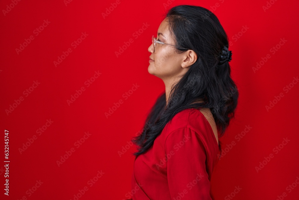 Asian young woman standing over red background looking to side, relax profile pose with natural face and confident smile. Asian young woman standing over red background looking to side, relax profile pose with natural face and confident smile.