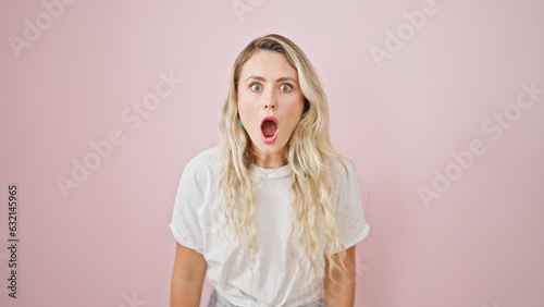 Young blonde woman standing with surprise expression over isolated pink background