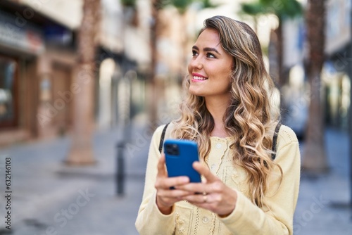 Young woman tourist smiling confident using smartphone at street