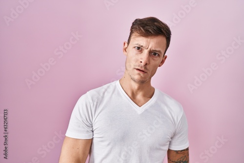 Caucasian man standing over pink background in shock face, looking skeptical and sarcastic, surprised with open mouth
