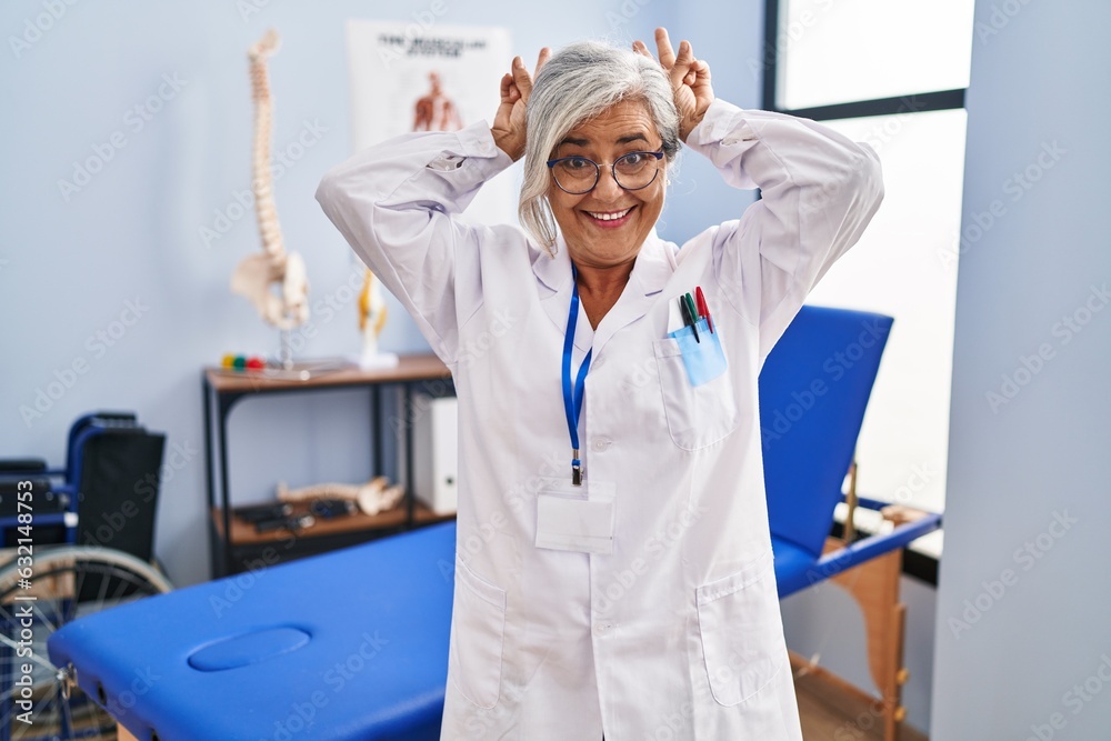 Middle age woman with grey hair working at pain recovery clinic posing funny and crazy with fingers on head as bunny ears, smiling cheerful Middle age woman with grey hair working at pain recovery clinic posing funny and crazy with fingers on head as bunny ears, smiling cheerful