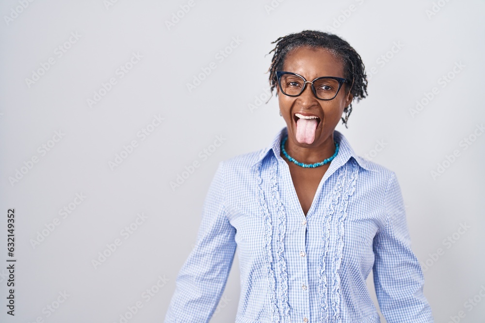 African woman with dreadlocks standing over white background wearing glasses sticking tongue out happy with funny expression. emotion concept. African woman with dreadlocks standing over white background wearing glasses sticking tongue out happy with funny expression. emotion concept.